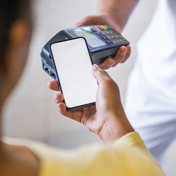 Woman in yellow shirt scanning phone for payment to a dentist in white scrubs