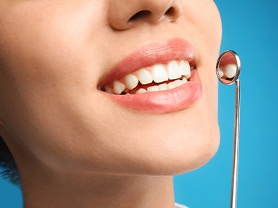 Nose to neck view of woman smiling with dental mirror held to teeth with blue background