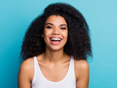 Woman in white tank top with curly hair smiling in front of blue background