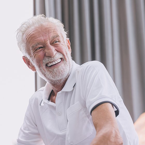 Senior man sitting on couch and smiling after full mouth reconstruction in Boston, MA